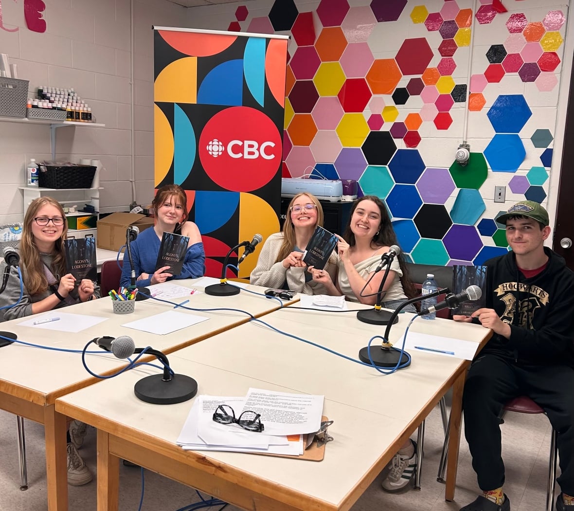 A group of teenagers around a table holding copies of a book with a CBC logo behind them.