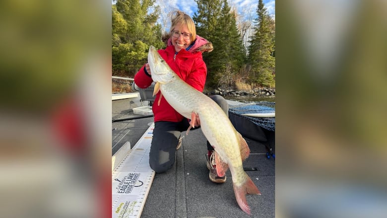 A woman smiles while holding a large muske she caught.
