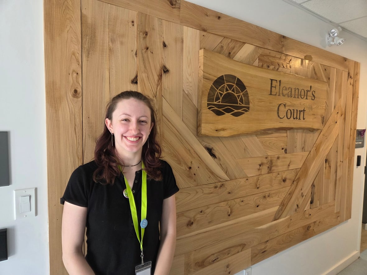 Bryanna MacLean stands in front of a large plaque reading "Eleanor's Court" made from trees cut down to make way for the new housing complex.