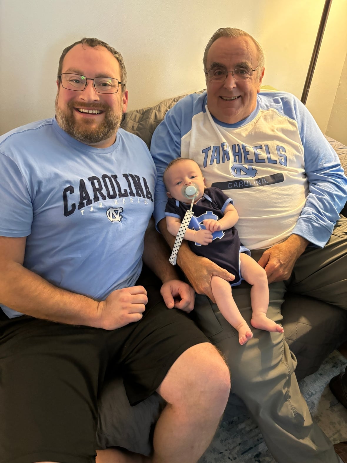A younger and older man sit with a baby