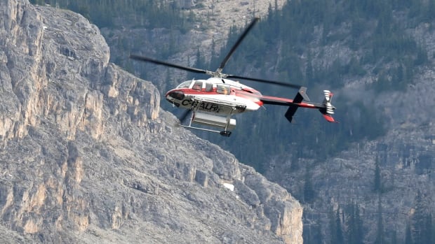 A helicopter is shown close to the scene of a rock slide near Bow Glacier Falls north of Lake Louise, Alta., in Banff National Park on June 19, 2025. a helicopter flies in front of a mountainside