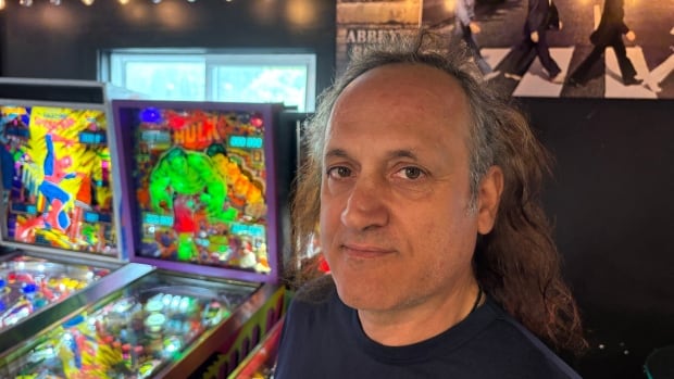 Rob Illuiri played pinball at arcades in Montreal throughout the 70s and 80s. Man stands in front of arcade game.