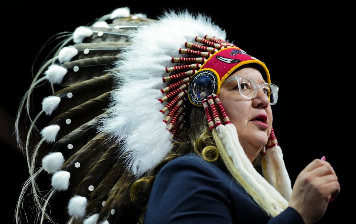 A woman wearing a headdress speaks into a microphone