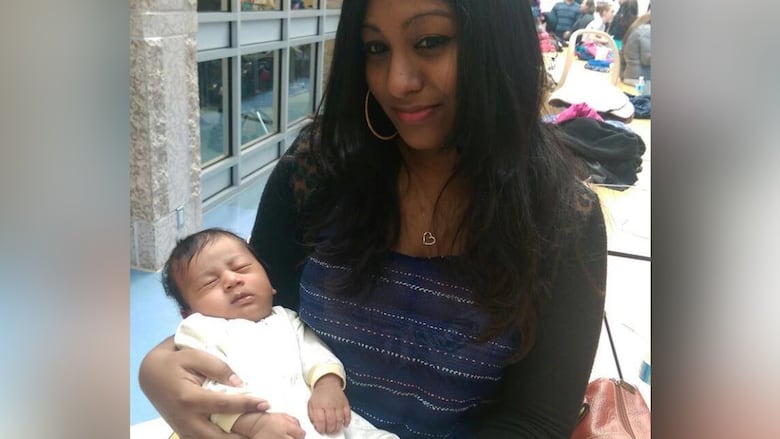 A woman with black hair holds a swaddled infant on her lap.