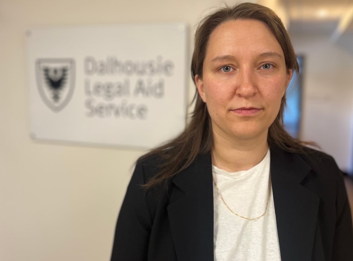 A woman in a white shirt and black jacket stands in from of a sign that says Dalhousie Legal Aid Service.