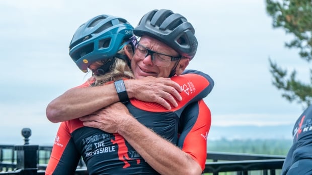 Two cyclists are seen hugging outside.