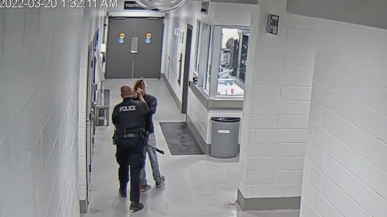 A police officer leads a man down a hallway by his hair.