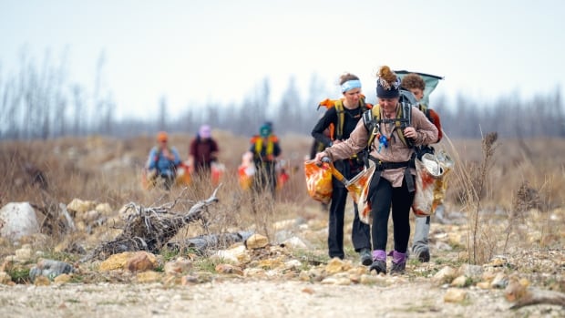 A group of people some holding orange bags are walking in an open field.
