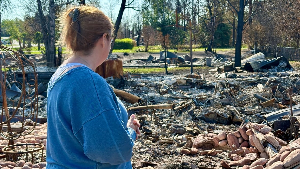 A woman in a blue shirt looks on at rubble.