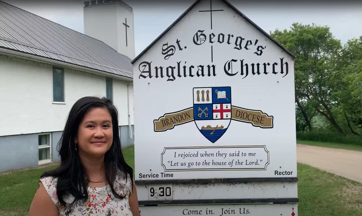 A smiling woman stands in front of a sign for a church.