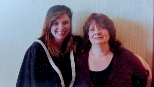 A woman in a graduation robe stands with her arm around an older woman
