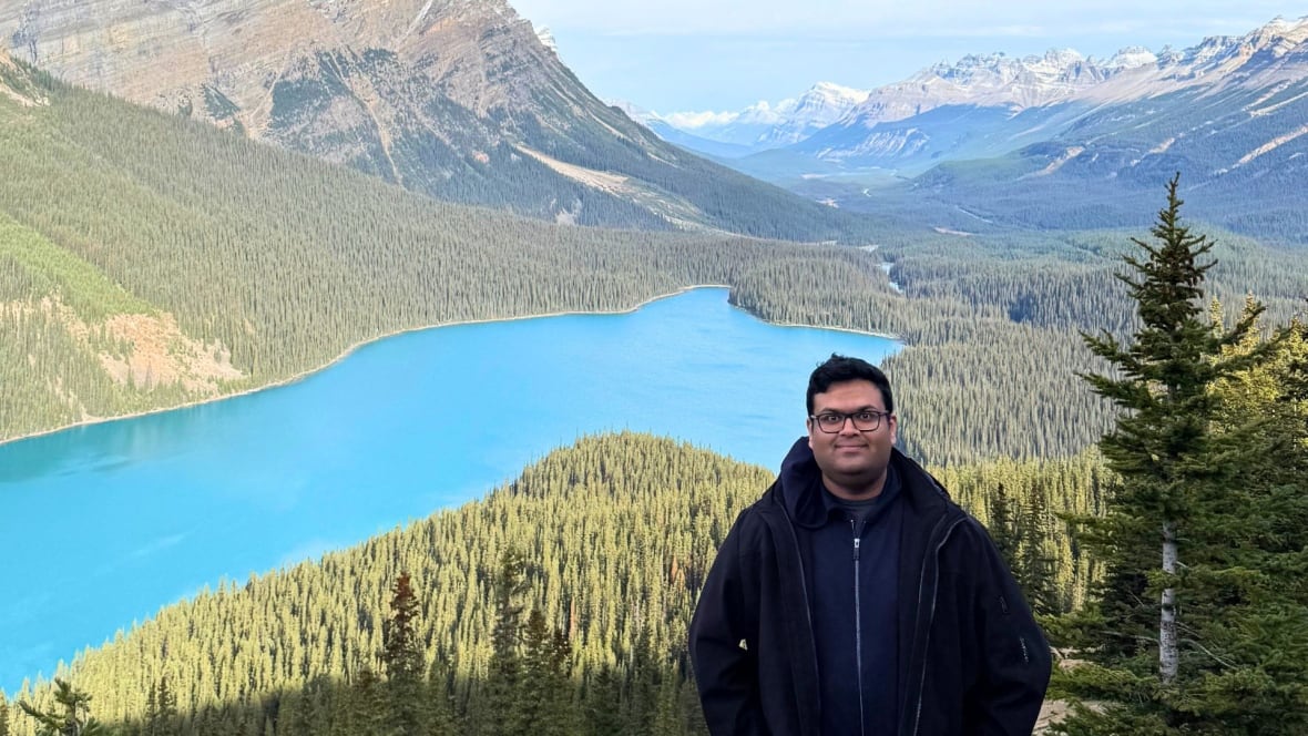 A man stands in front of a beautiful blue lake in the mountains.
