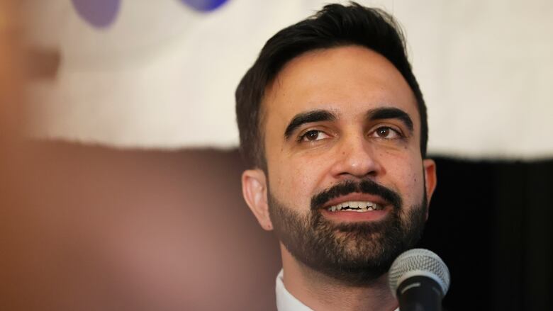 A bearded dark haired man smiles in a closeup photo.