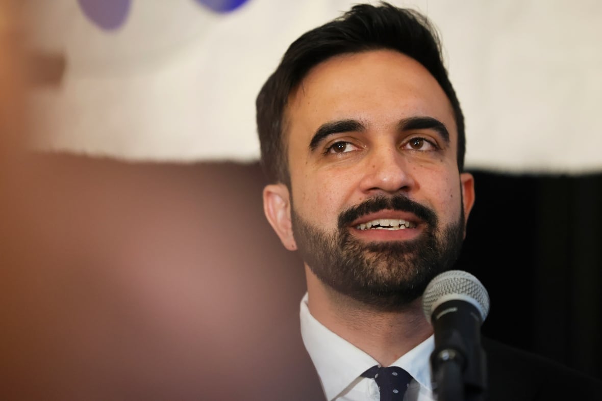 A bearded dark haired man smiles in a closeup photo.