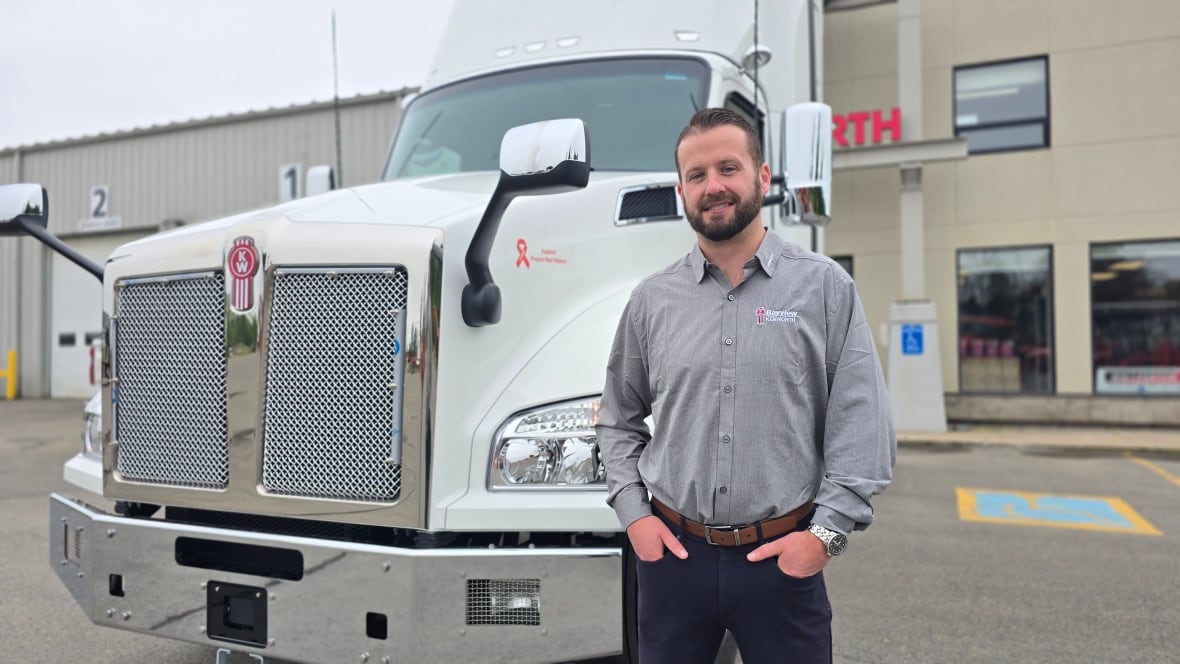 Man in a grey shirt standing in front of a white transport truck.