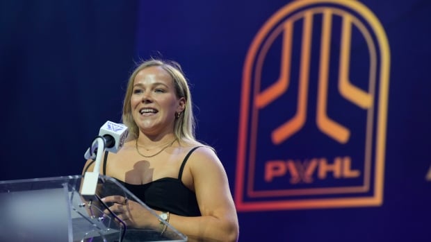 A woman speaks at a podium, with a PWHL logo in the background.