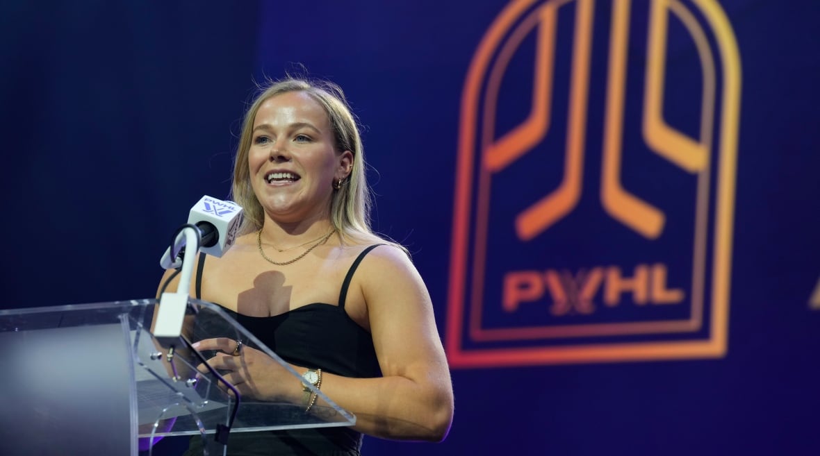 Eine Frau spricht an einem Podium, im Hintergrund ist ein PWHL-Logo zu sehen.