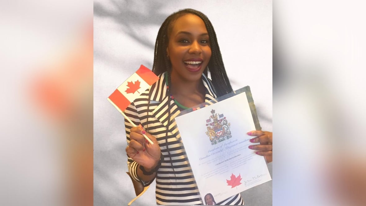A smiling Black woman with long braids as she waves a paper Canadian flag and a Canadian citizenship certificate.