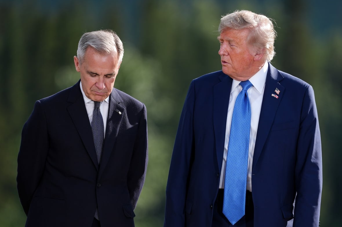 Two men in suits stand side by side. One is looking at the other, whose eyes are downcast.