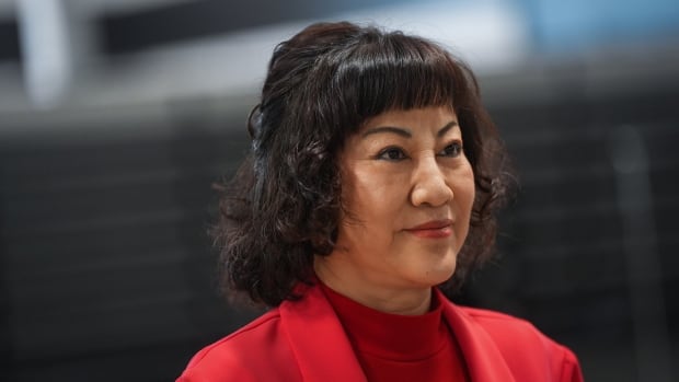 An East Asian woman with a dark bob haircut and red lipstick, wearing a red top and matching red blazer.