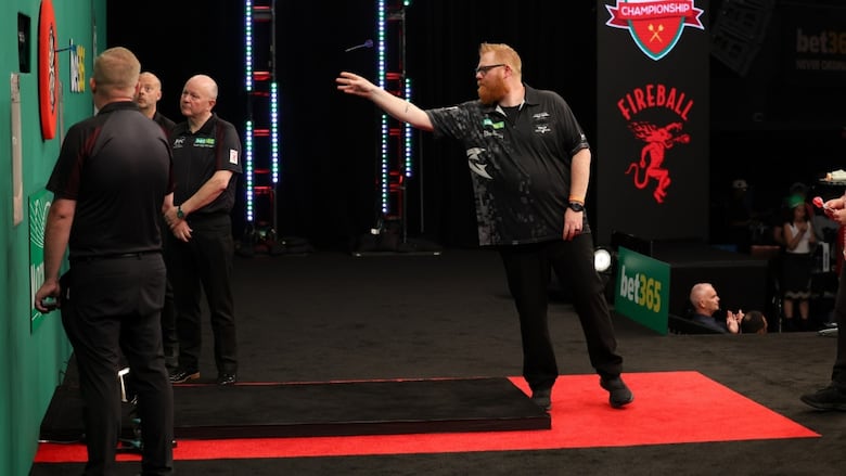 Male darts players extends arm to throw dart.