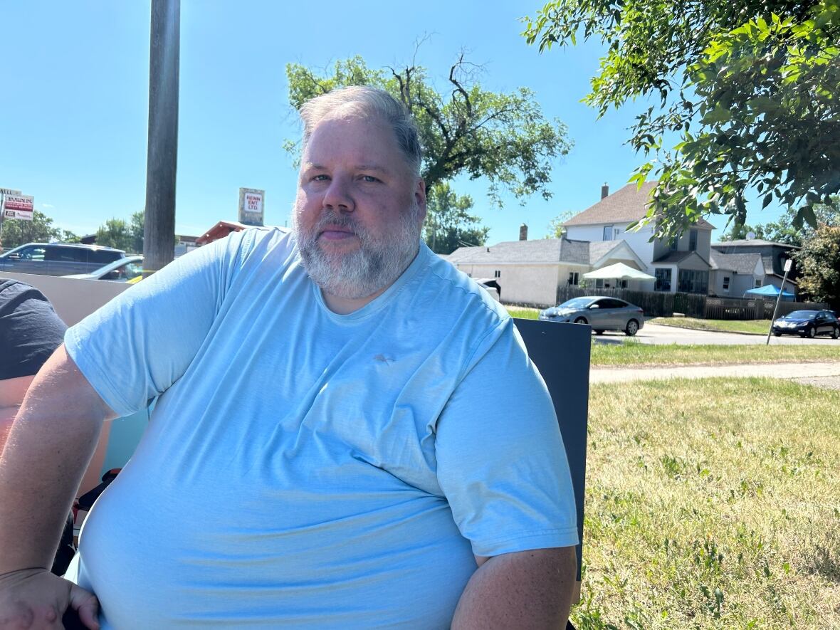A man in a blue shirt is seen sitting on a chair outside 