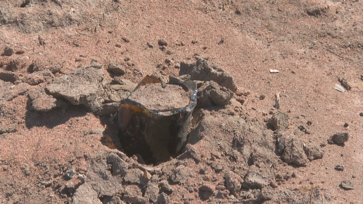 A broken piece of brown beer bottle pokes up out of the small chunks of hardened sand.