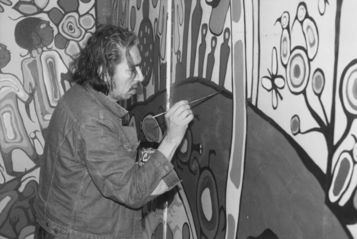 A black and white image shows a man in a jean jacket. He's visible from the side, painting on a wall in front of him. He appears to be concentrating on a line he's painting.