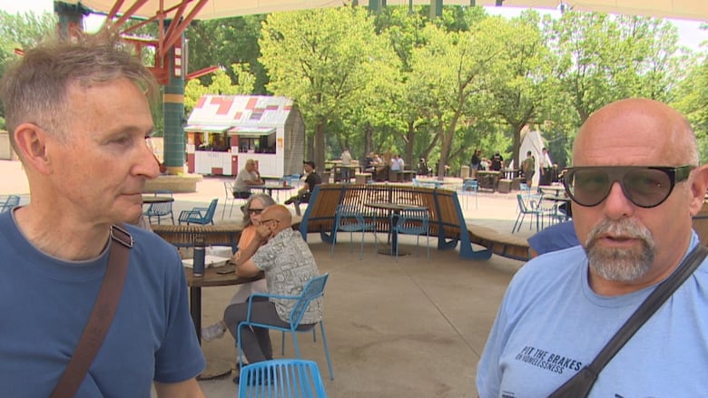 Man with grey hair and dark blue t-shirt looks at bald man with grey facial hair wearing a light blue t-shirt