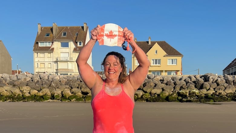 Aerin Bowers poses on a beach with holding a swimming cap coloured as the Canadian flag above her head.