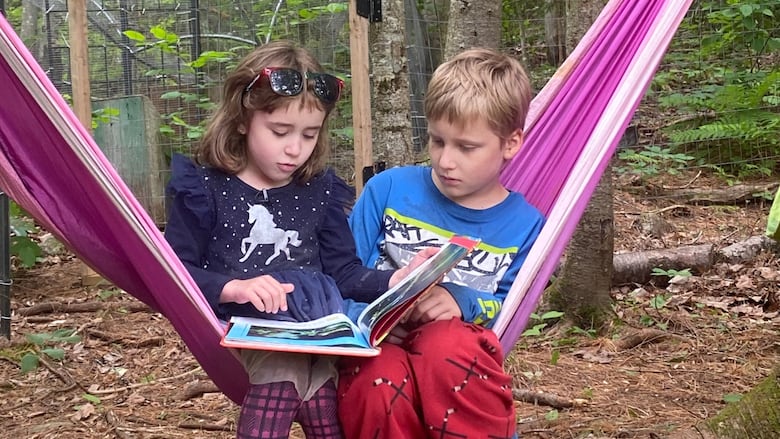 a little girl and boy read on their hammock in a back yard