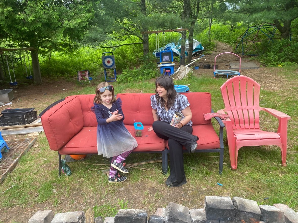 A little girl shows off her caterpillars to her mother as they sit on a couch in their back yard.