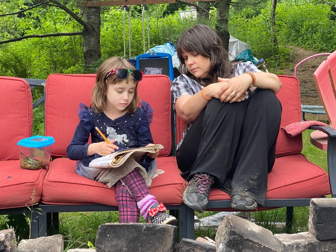 A little girl does match exercises in a workbook with her mother on a couch in their back yard.