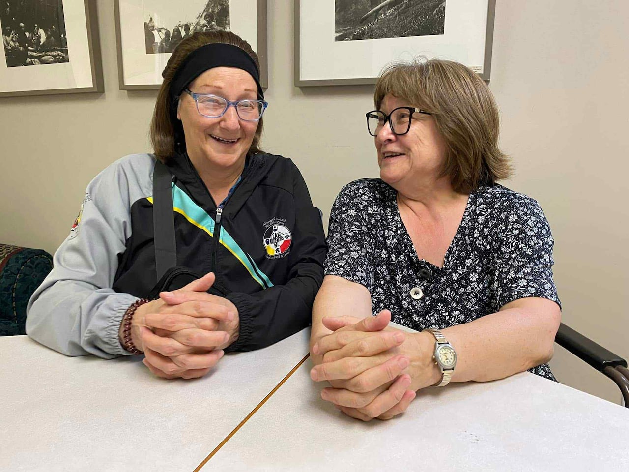 Two Inuk women sit at a table smiling and laughing