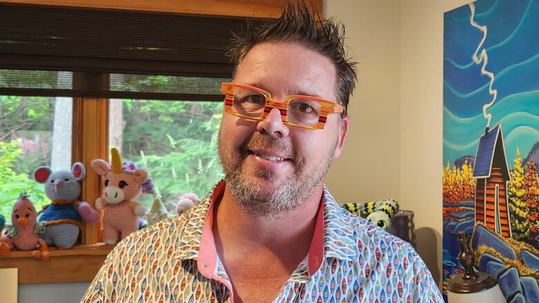 A antheral   with colourful glasses smiles astatine  the camera.