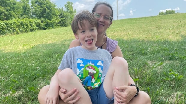 A boy sits on his mother's lap on a grassy hill.