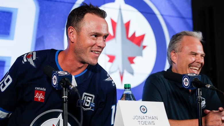 A man smiles with a hockey jersey on.