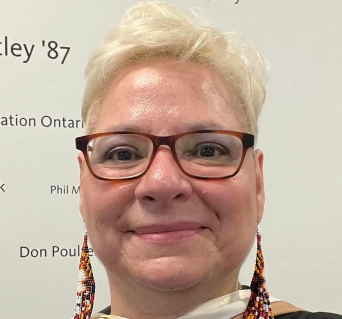 A woman with short blonde hair and beaded earrings seen in a headshot 