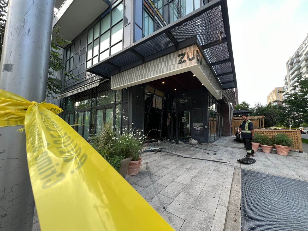 Photo showing a restuarant in a downtown area with a damaged exterior. There is glass and debris on the ground.
