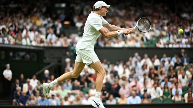 A men's tennis player is shown returning a shot while in mid air.