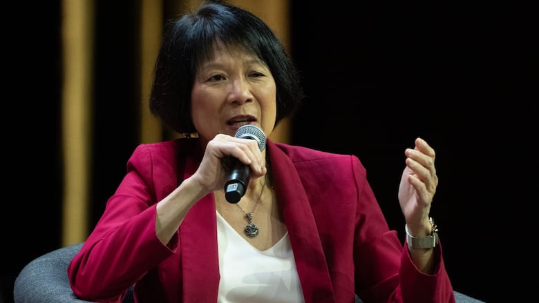 Photo of a woman wearing a red blazer and white shirt speaking into a microphone