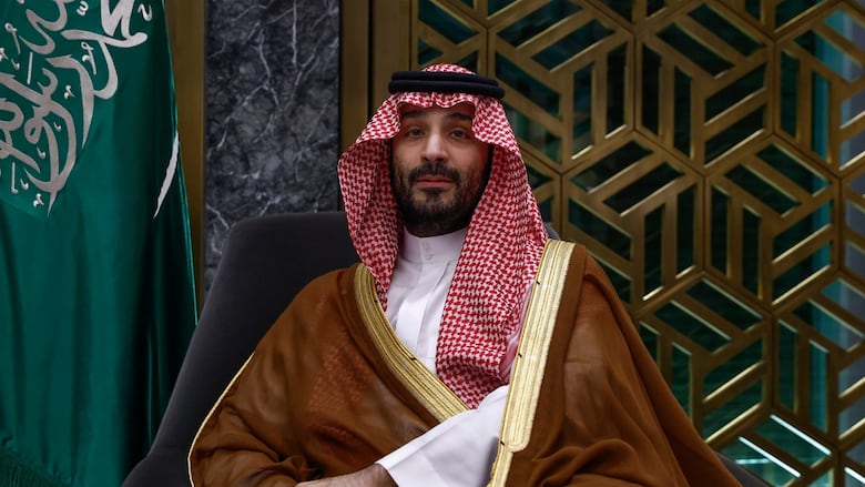 A bearded man in an Arabic headress and robes is shown.