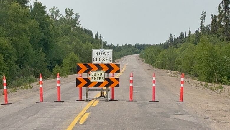 A 'road closed' and 'do not enter' sign blocks the path on a highway lined by forest.