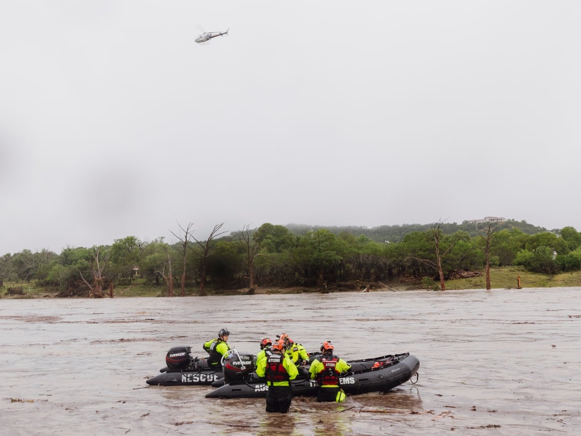 People in hi-vis gear and helmets in an inflatable black boat as helicopter flies overhead