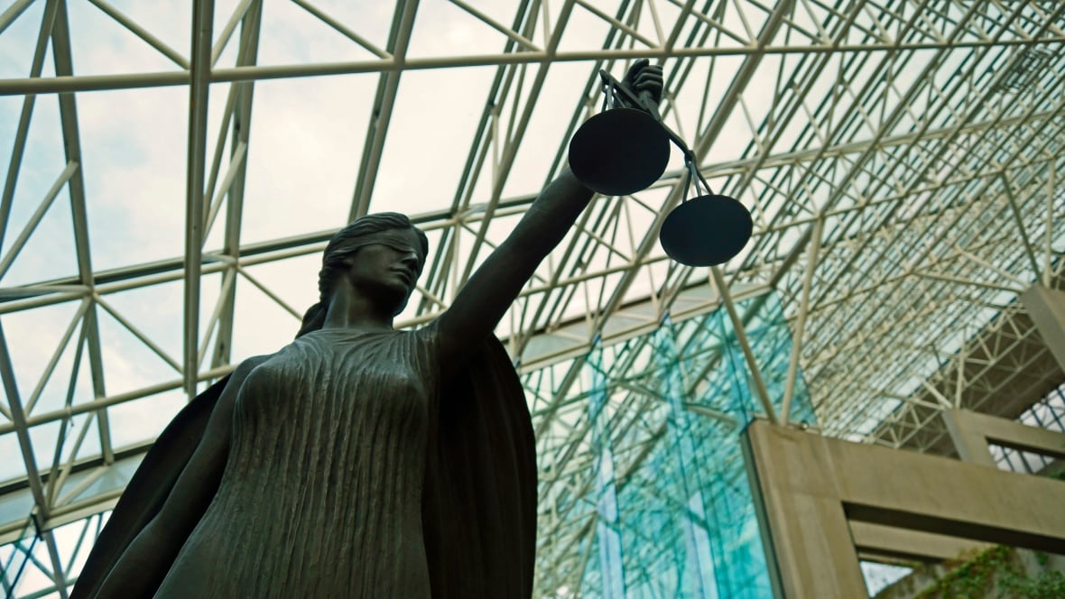 A statue of a blindfolded female figure holding a scale inside a glass-roofed building