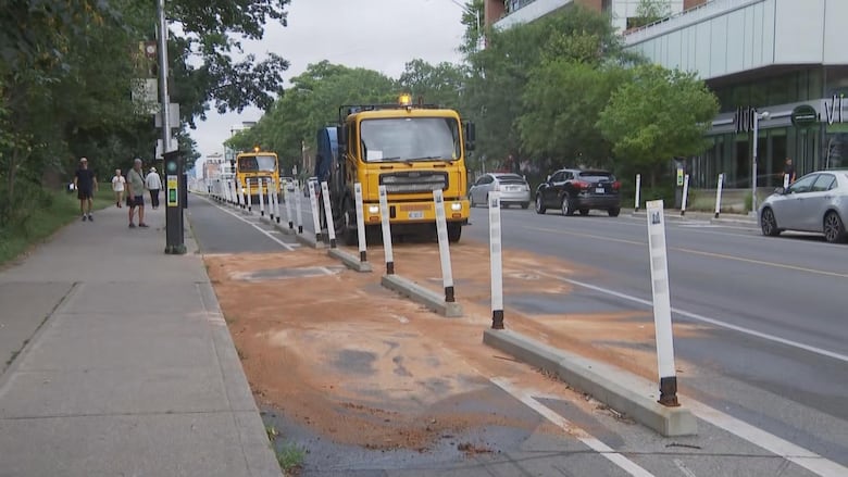 A yellow truck cleaning up a brown spill on a roadway in a city