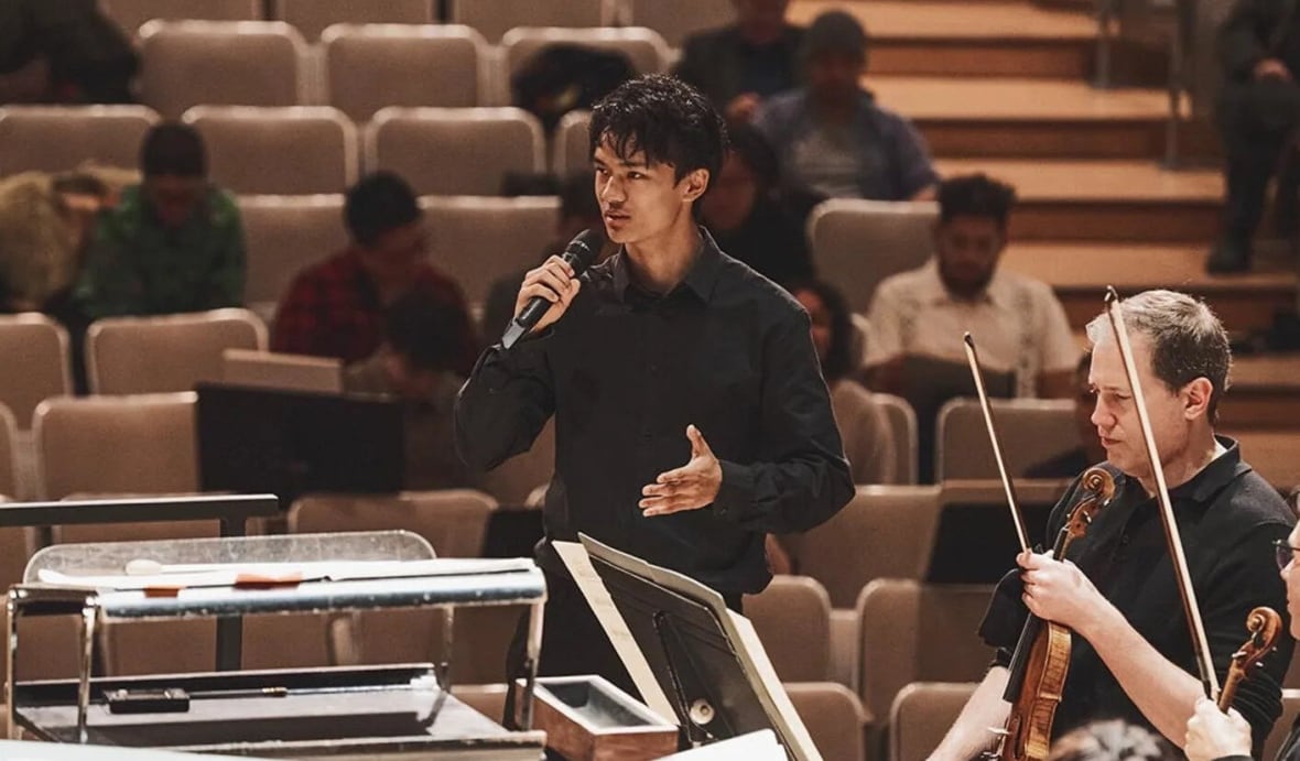 Composer Sky Yang speaks into a microphone during a symphony rehearsal.