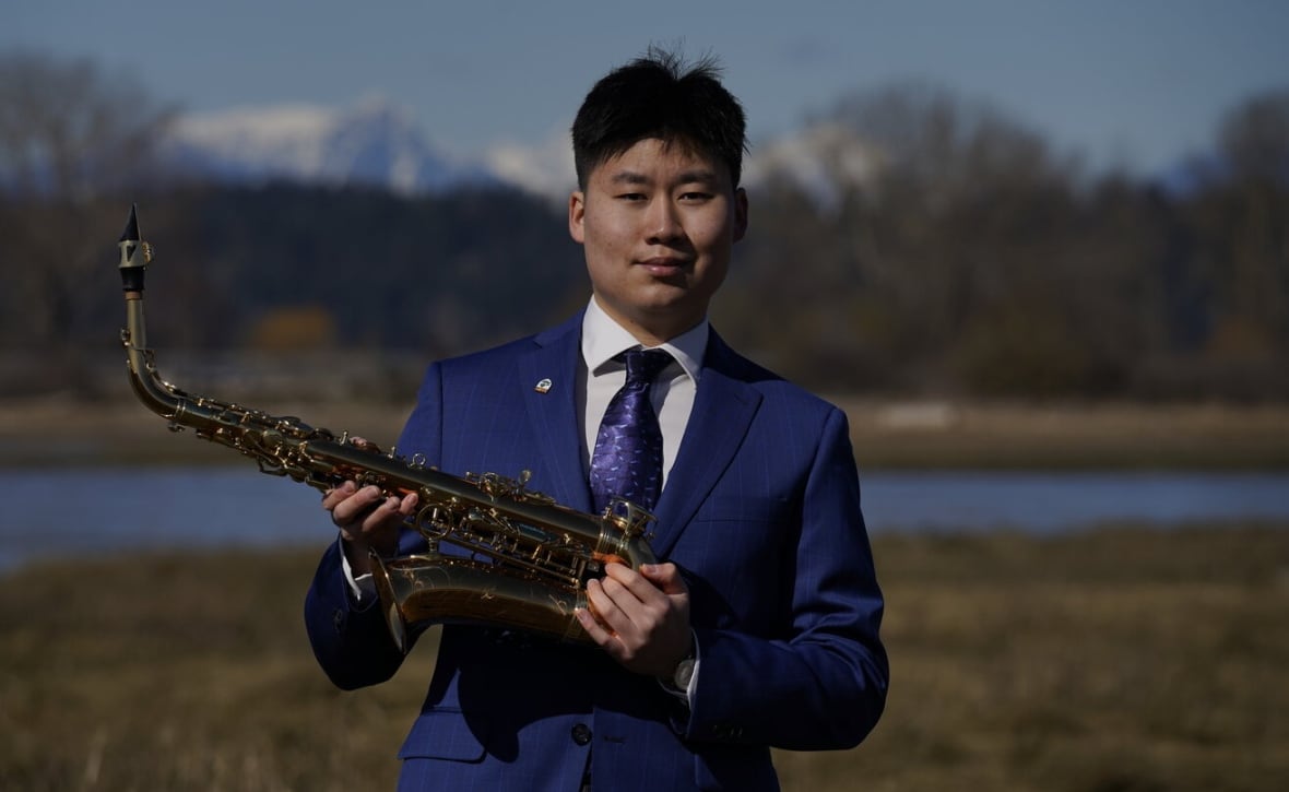 Sunny Wu poses outdoors with his saxophone.