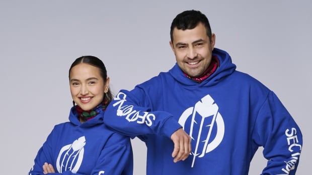 Two people smiling in black pants and runners and blue hoodies. 