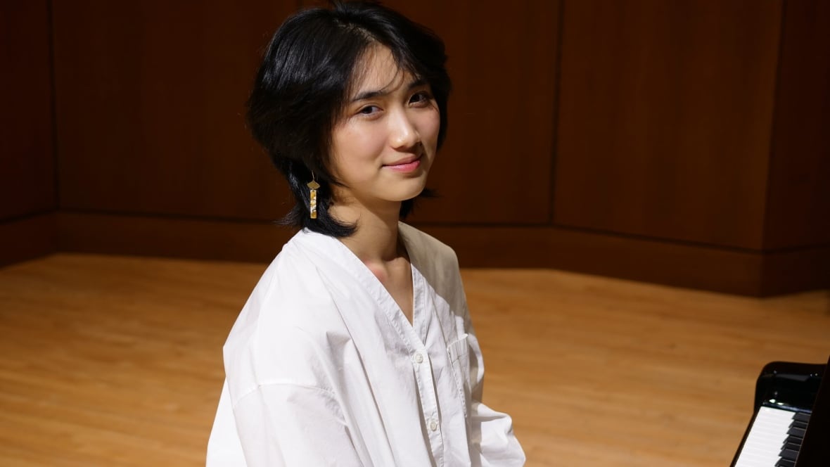 Athena Deng, wearing a white shirt, sits at the piano.